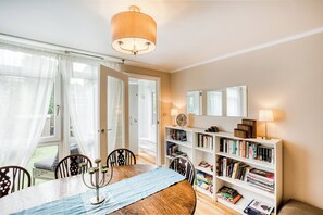 Un coin repas comprenant une table, des chaises, un chandelier et une bibliothèque avec des livres et une horloge.