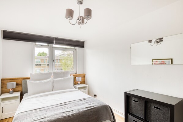 Une chambre moderne avec un lit, des tables de chevet, une commode, une fenêtre avec des stores et un luminaire au plafond.
