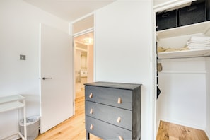 Une pièce avec un plancher en bois, une commode grise dotée de tiroirs, une porte blanche et un placard avec des étagères.
