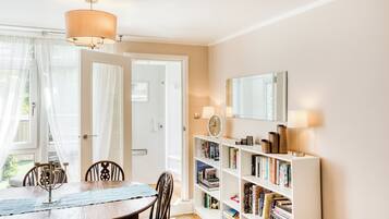 A dining area with a table and chairs, a bookshelf with books, a clock, and a mirror on the wall.