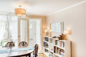 Un coin repas avec une table et des chaises, une bibliothèque remplie de livres, une horloge et un miroir accroché au mur.