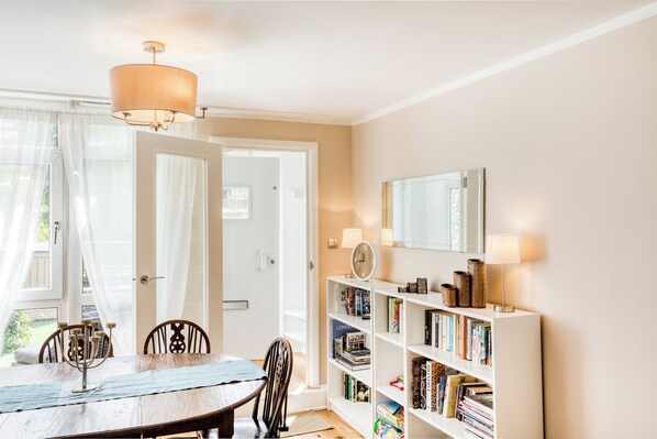 A dining area with a table and chairs, a bookshelf with books, a clock, and a mirror on the wall.