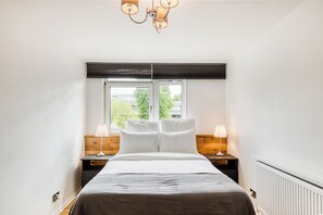 Ein Schlafzimmer mit einem Bett, zwei Nachttischen, einem Fenster und einer Deckenleuchte.