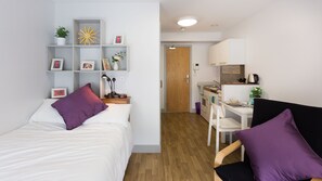 A compact studio apartment with a bed, a desk, a kitchenette, and a small dining area. - Unilife High Street (Southampton)