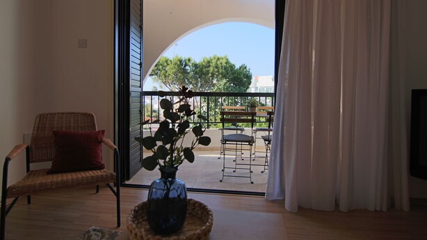 A room with a wicker chair, a red cushion, and a vase with green plants on a wooden floor. - Phaedrus Living: Luxury Flat Protaras Sea View 9 (Paralimni)