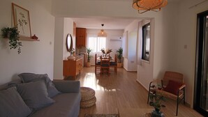 A spacious living room with a sofa, a dining area with a table and chairs, and a wicker chair. - Phaedrus Living: Luxury Flat Protaras Sea View 9 (Paralimni)