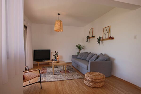 A living room with a grey sofa, a television, a wicker chair, a wooden coffee table, and a hanging light fixture.