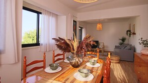 A dining area with a wooden table, chairs, and a vase with dried plants. There is a sofa and a lamp in the background. - Phaedrus Living: Luxury Flat Protaras Sea View 9 (Paralimni)