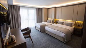Ein Hotelzimmer mit zwei Betten, einem Schreibtisch, einem Sessel und einem Fernseher.