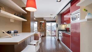 A modern kitchen with a central island, white bar stools, and red cabinetry.