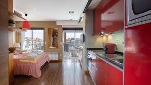 A modern kitchen with red cabinets, a wooden floor, and a view through a glass door to the outside.