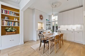 A modern kitchen with white cabinetry, a dining table with chairs, and a bookshelf filled with books.