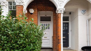 A traditional building with a white facade, a brick entrance, and a black door. - Beautiful 2BD Flat with Private Garden, Clapham (London)