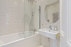 A modern bathroom with a glass-enclosed shower, a white bathtub, and a sink with a mirror above it.