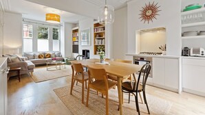 A modern living room with a dining area, a kitchen, and a bookshelf. - Beautiful 2BD Flat with Private Garden, Clapham (London)