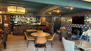 A cozy bar area with a stone wall, wooden ceiling, and a variety of seating options including round tables and chairs. - OYO Lamphey Hall Hotel (Pembroke)