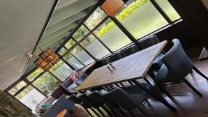 A modern dining area with a large table and chairs, large windows, and a stone wall. - OYO Lamphey Hall Hotel (Pembroke)