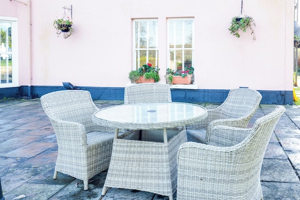 A round wicker table with six chairs, potted plants on the wall, and a window with blinds. - OYO Lamphey Hall Hotel (Pembroke)