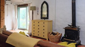 Ein gemütliches Zimmer mit einem Holzkasten, einem Spiegel, einem schwarzen Herd und einem Korbwägelchen.