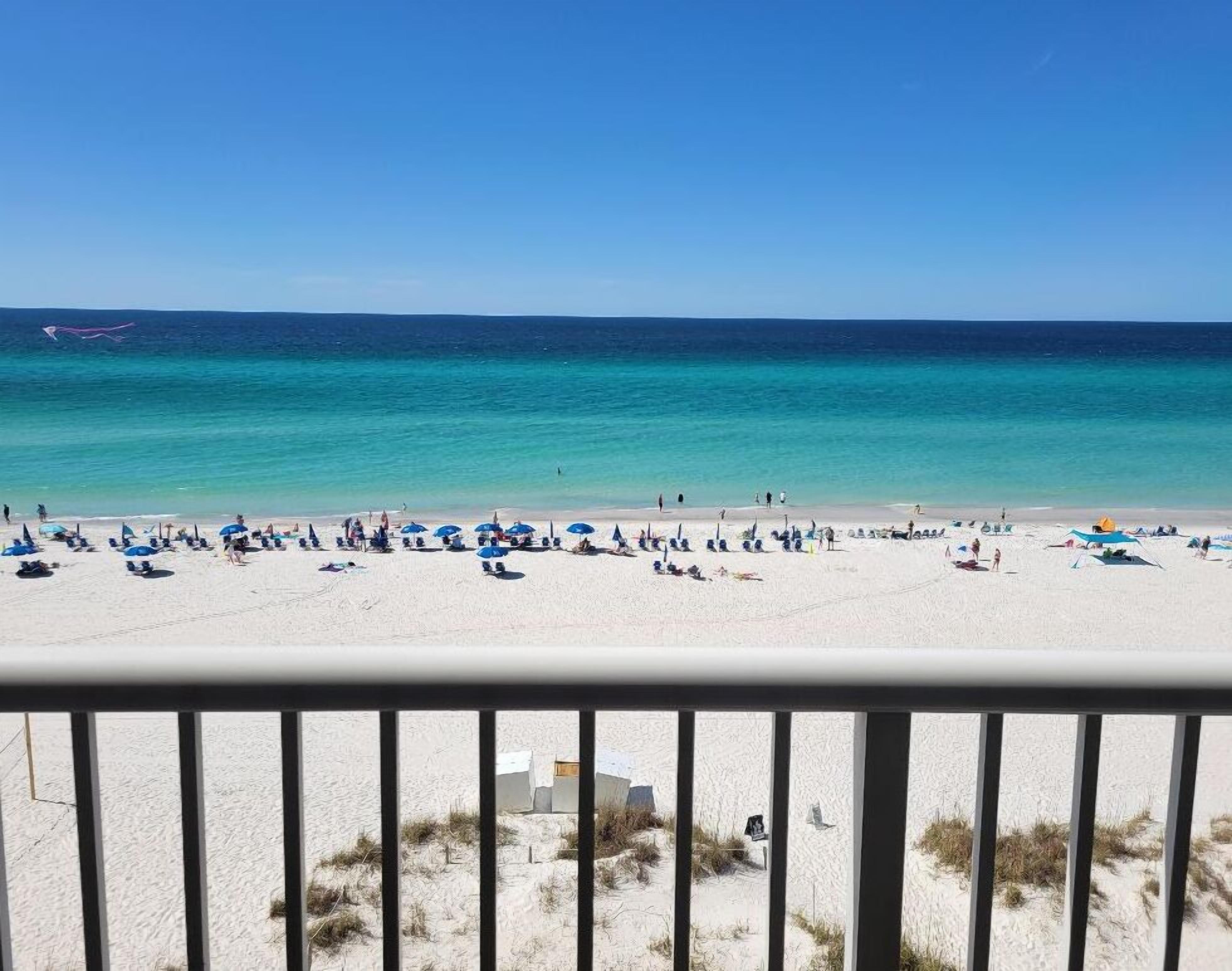 A beach with white sand and clear turquoise water. There are several umbrellas and people relaxing.