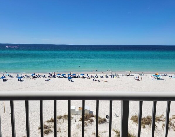 A beach with white sand and clear turquoise water. There are several umbrellas and people relaxing.