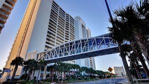 A modern hotel with a pedestrian bridge, palm trees, and high-rise buildings in the background. - # 505~BeachFront 5th Floor Movie Theater~ Pools ~ Game Rm~ Majestic Beach Resort (Panama City Beach)
