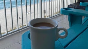 A balcony with a view of the beach and ocean, a white mug on a teal table, and a chair. - # 505~BeachFront 5th Floor Movie Theater~ Pools ~ Game Rm~ Majestic Beach Resort (Panama City Beach)