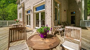 A wooden deck with outdoor furniture, a potted plant, and a brick building with large windows. - Wedding Venue - Maison D'artagnan on Pimmit Run - Great for Extended Stays (McLean)