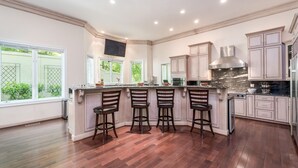 A spacious kitchen with a central island, bar stools, and a large window providing a view of the outdoors. - Wedding Venue - Maison D'artagnan on Pimmit Run - Great for Extended Stays (McLean)