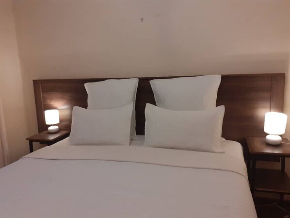A hotel room with a large bed, two bedside tables, and two wall-mounted lamps. - Charming 6-Bed House with Swimming Pool in Harare (Harare)