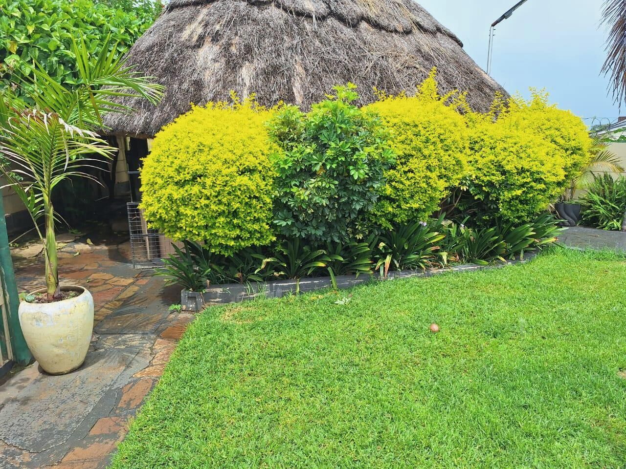 A thatched-roof structure surrounded by well-maintained greenery and a paved pathway.
