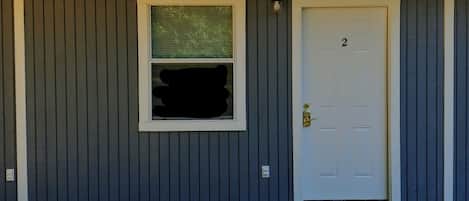 Un bâtiment avec une porte blanche portant le numéro 2, une fenêtre avec un écran vert et un toit en métal.