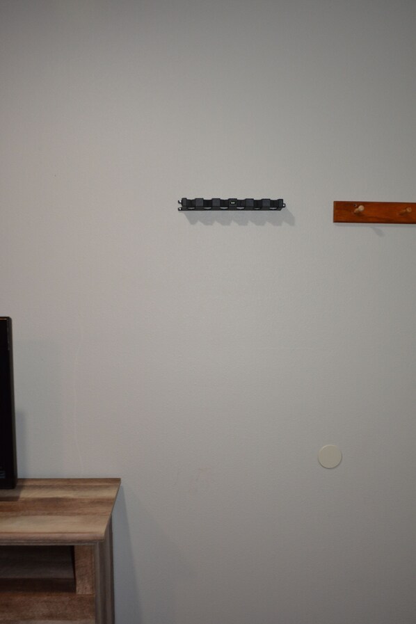 Eine Wand mit einem schwarzen Gegenstand, einem Holzregal und einer runden Leuchte.
