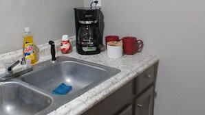 A kitchen with a double sink, a coffee maker, a bottle of Ajax dish soap, and a red mug. - Apartment 2- 2760 Carters Ferry Road Milam Texas.        Free Ice !!!  (Milam)