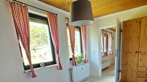 A bedroom with a large bed, wooden ceiling, and red and white checkered curtains.