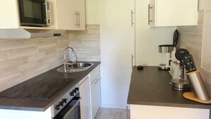 A compact kitchen with white cabinetry, a microwave, a sink, and a coffee maker.