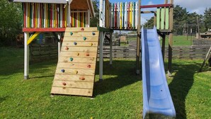 A playground with a climbing wall, a slide, and a small wooden house structure.