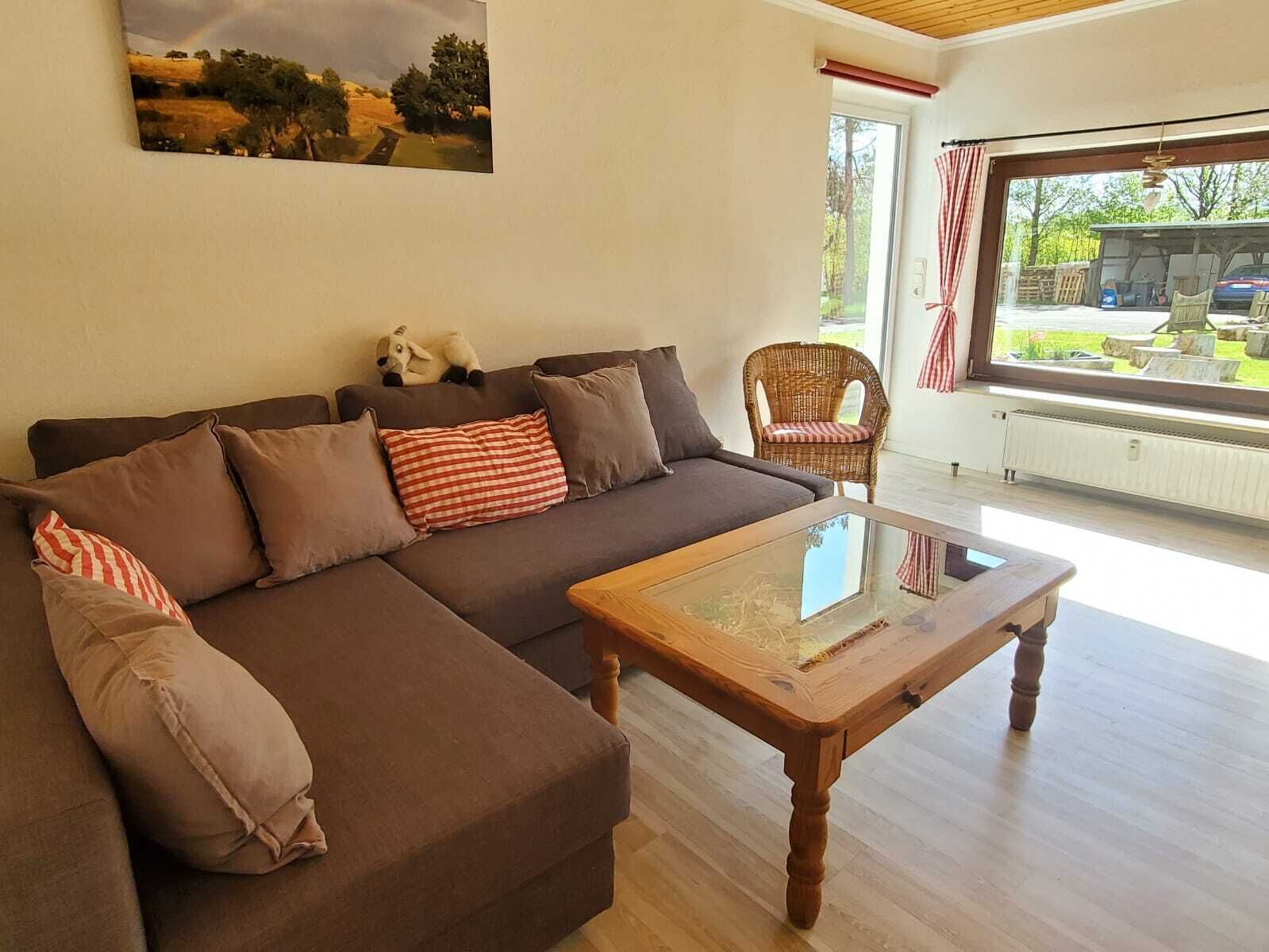 Uma sala de estar com um sofá seccional marrom, uma mesa de centro de vidro e uma cadeira de vime.