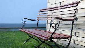 A wooden bench with metal armrests and legs, positioned on grass in front of a wooden building. - Vacation apartment "Eselstube"! Vacation on a farm in the Eifel (Nettersheim)