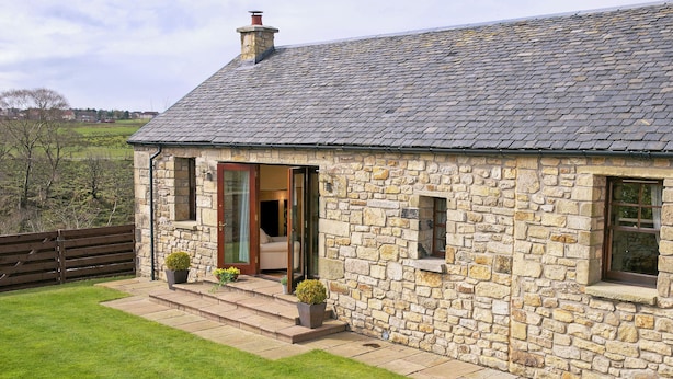 Une maison en pierre avec un toit en tuiles, une porte en bois et un petit porche agrémenté de plantes en pot.