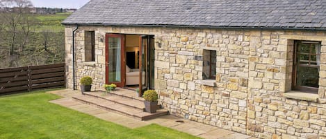 A stone house with a tiled roof, a wooden door, and a small porch with potted plants.