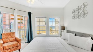Un dormitorio con una cama grande, una silla y vistas a edificios a través de las ventanas.