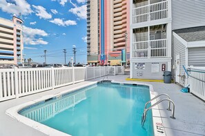Una piscina profonda 1 metro e 20, circondata da una recinzione bianca, adiacente a un edificio con balconi e una postazione di salvataggio.