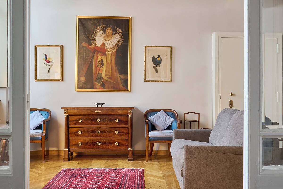 Una sala de estar con un aparador de madera, dos sillones, un sofá y tres cuadros en la pared.