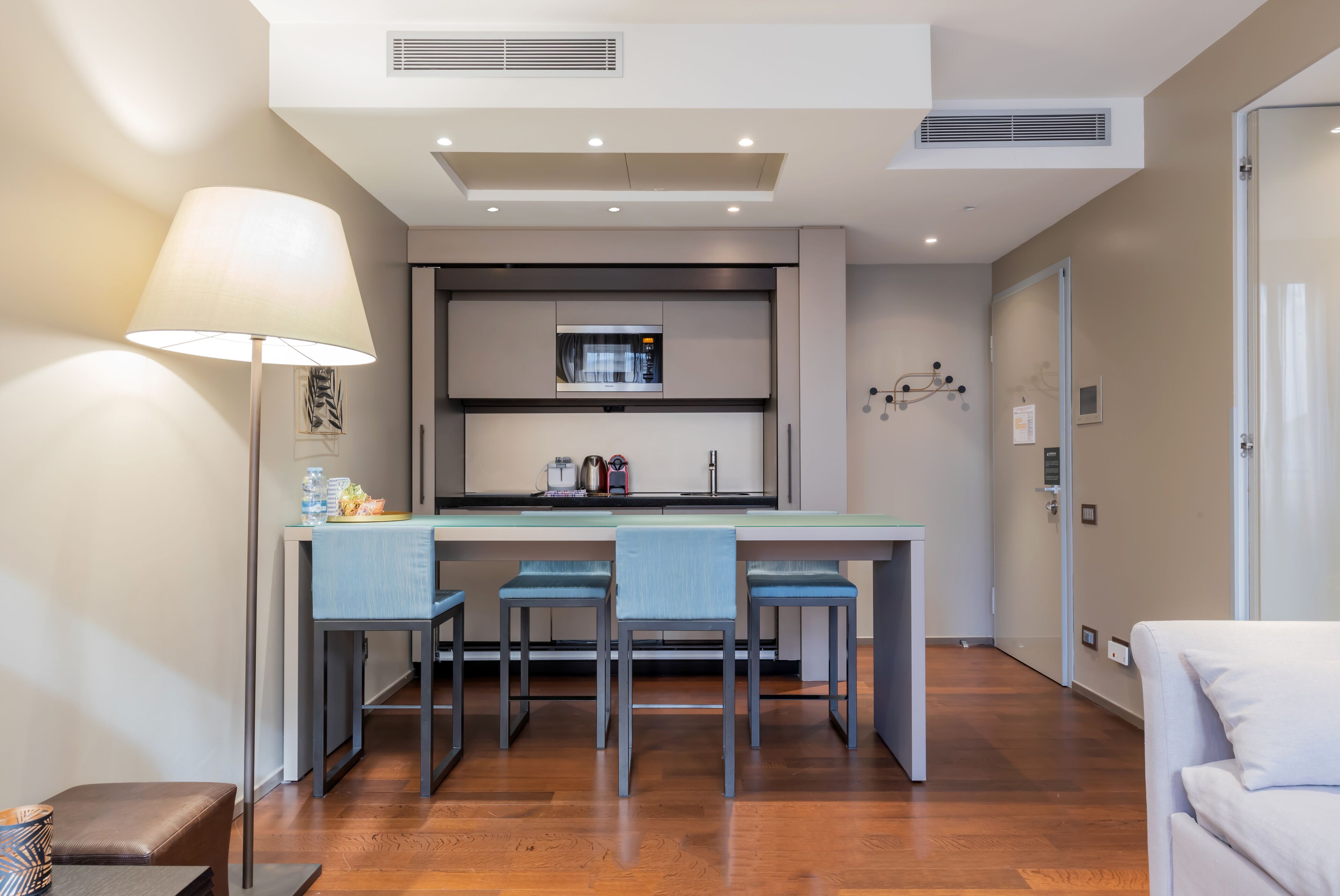 A modern kitchen with a central island, three bar stools, and a dining table.