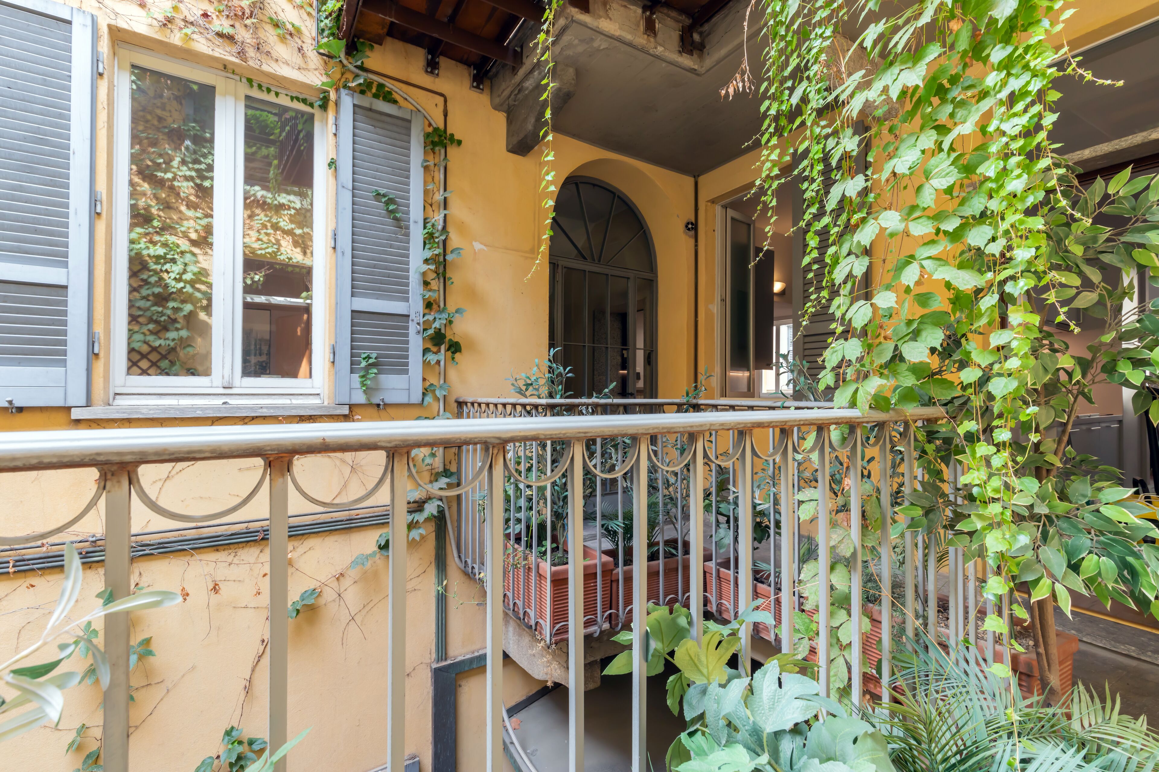 Een balkon met een sierhekwerk, plantenpotten en een gele muur.
