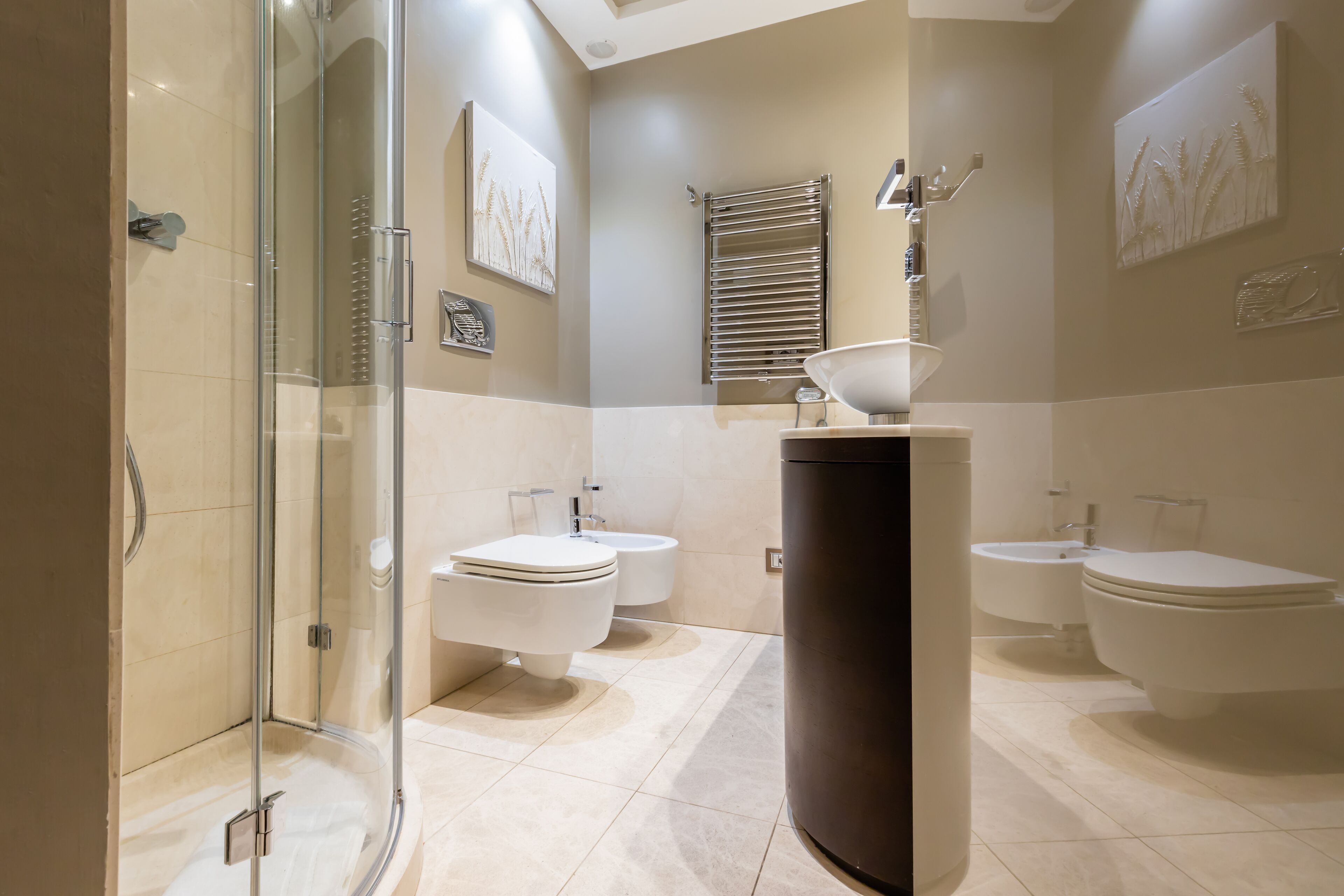 Ein modernes Badezimmer mit einer gläsernen Duschkabine, zwei Toiletten, einem Bidet und einem großzügigen Waschtisch.