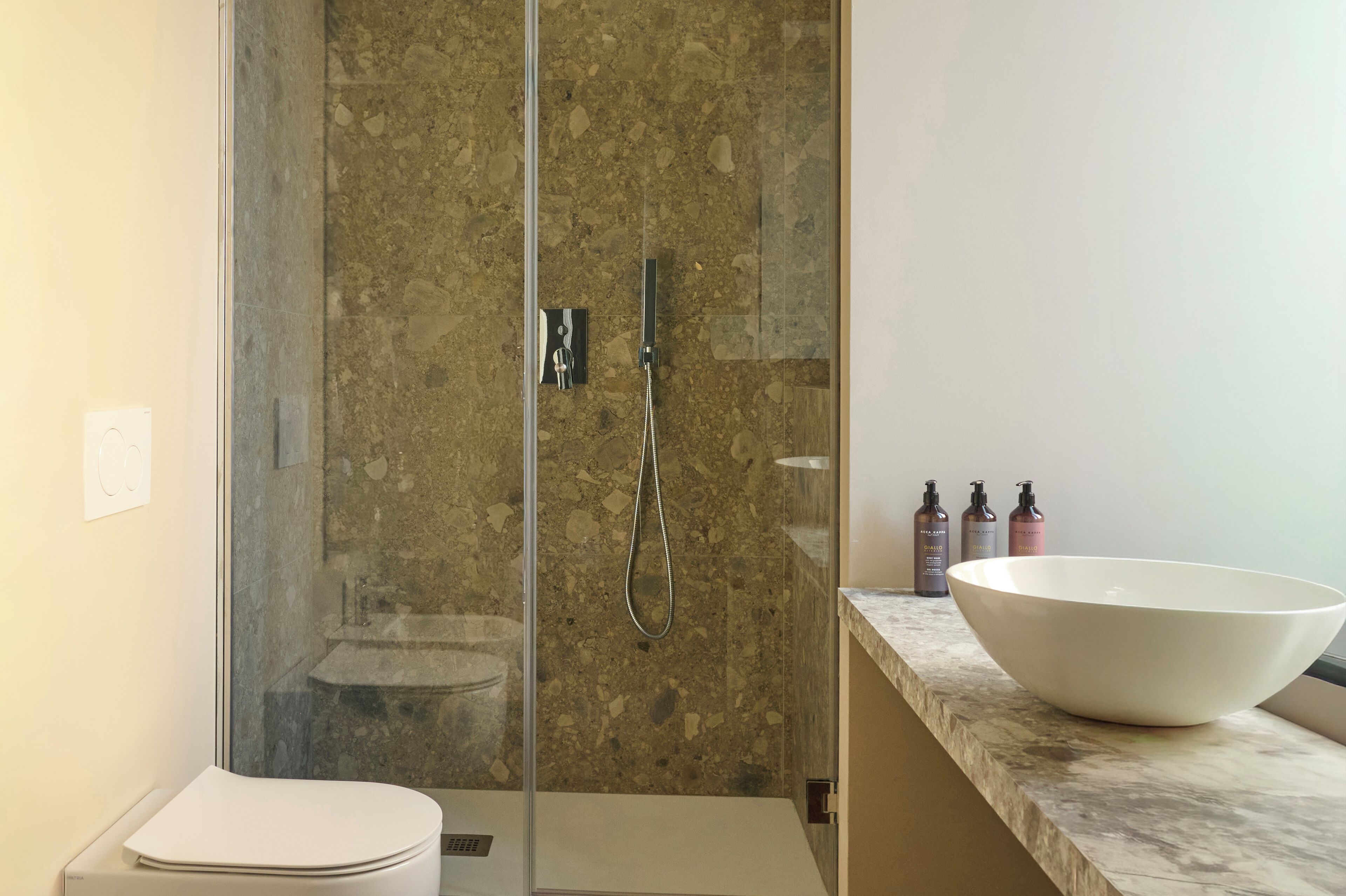 A modern bathroom with a glass-enclosed shower, a white sink, and toiletries on the countertop.