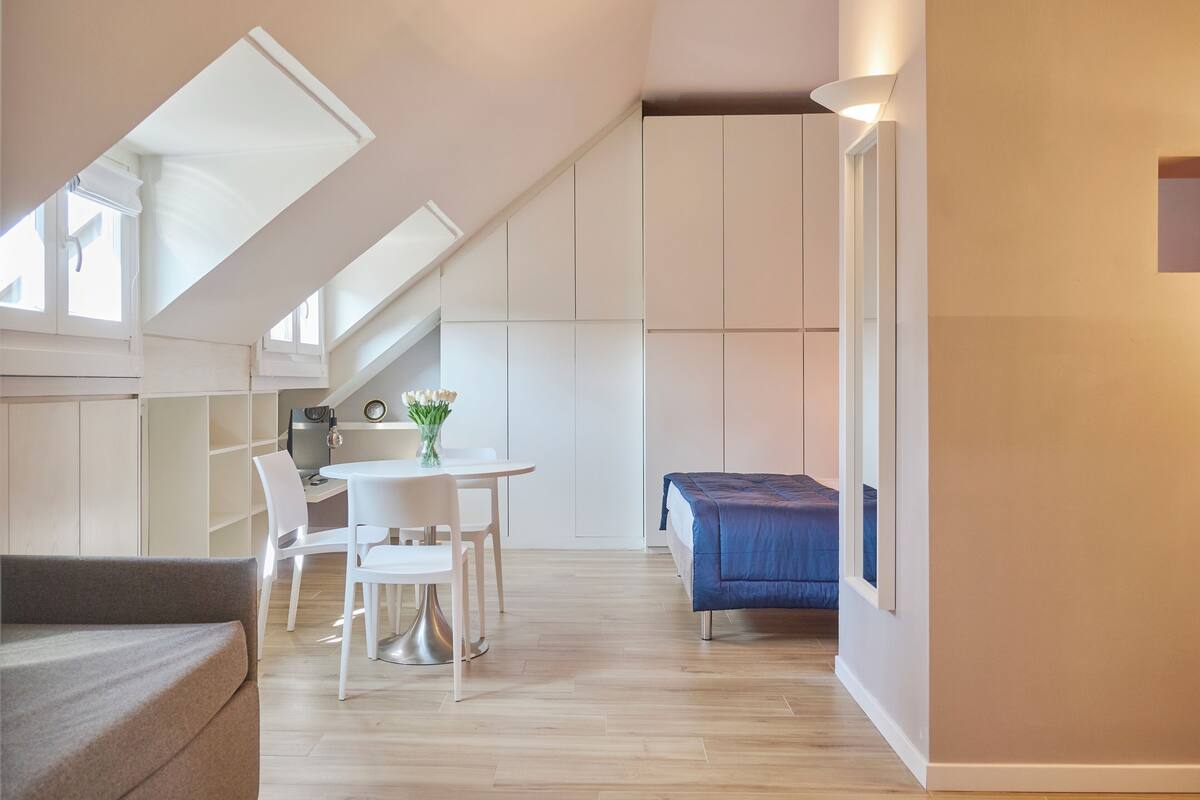 Un espacio habitable moderno y funcional con comedor, cama pequeña y kitchenette.