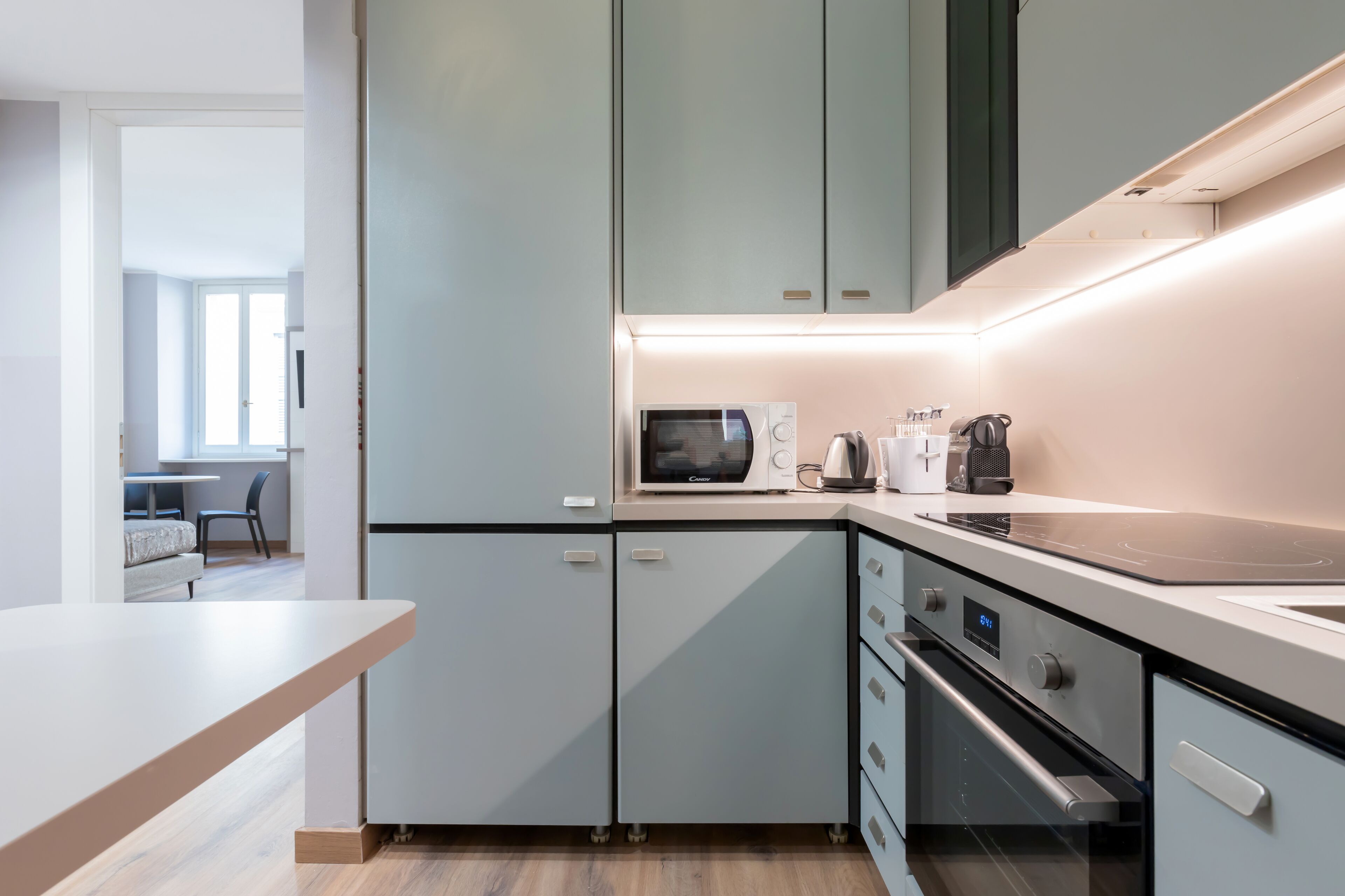 Une cuisine moderne avec des meubles de couleur claire, un four à micro-ondes encastré, une machine à café et une cuisinière.